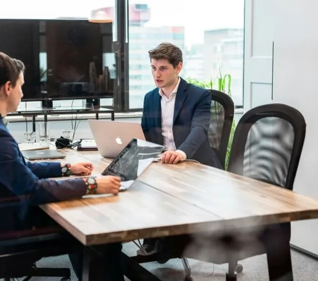 Twee mannen in pak overleggen aan een tafel met laptops