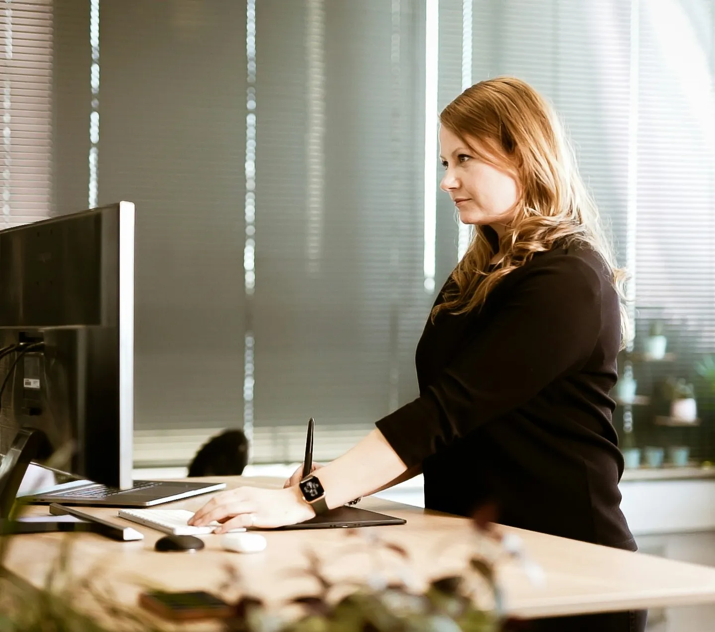 Een vrouw werkt staand aan een bureau met een beeldscherm en een tekentablet
