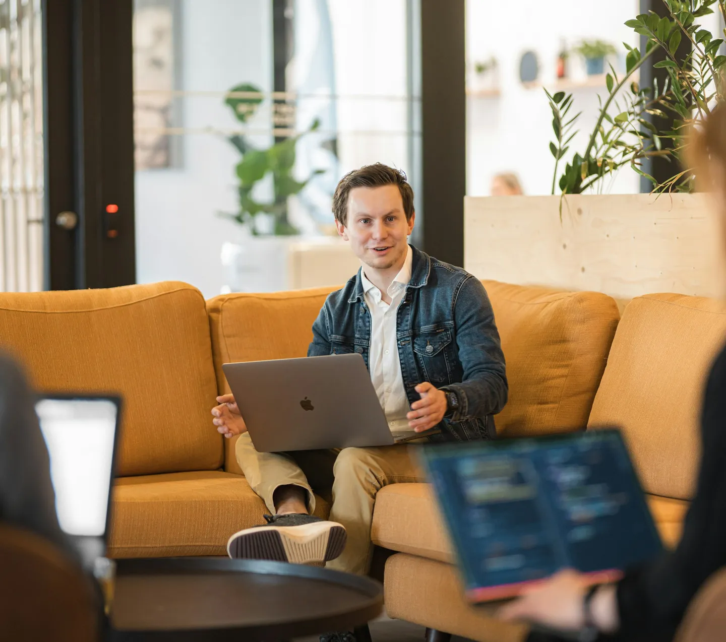 Een man met een laptop op schoot praat vanaf een gele bank