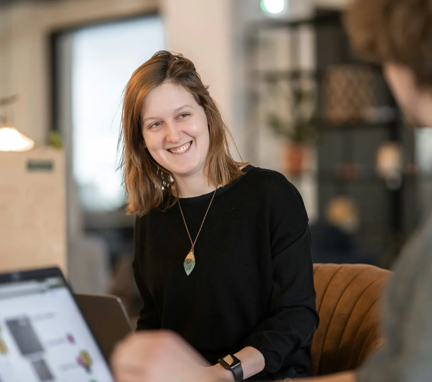 Een lachende vrouw in gesprek, met een laptop op de voorgrond