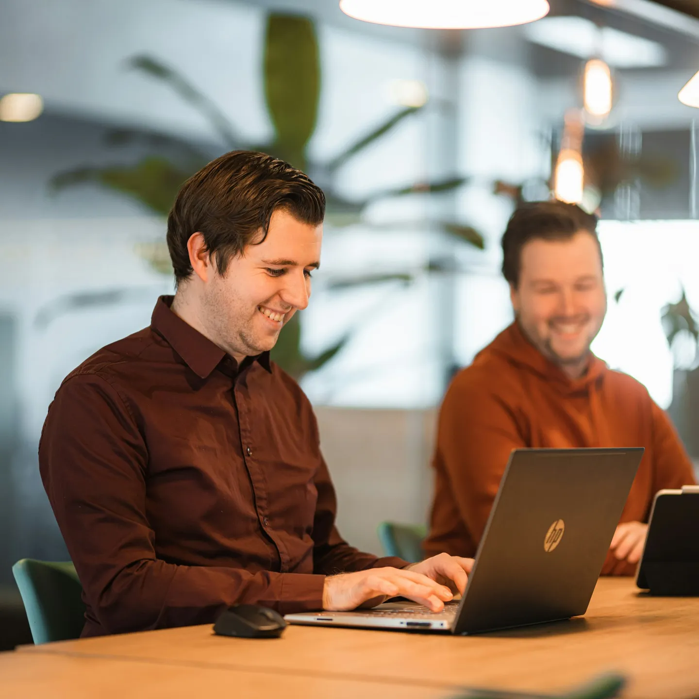 Two colleagues smiling while working on their laptops