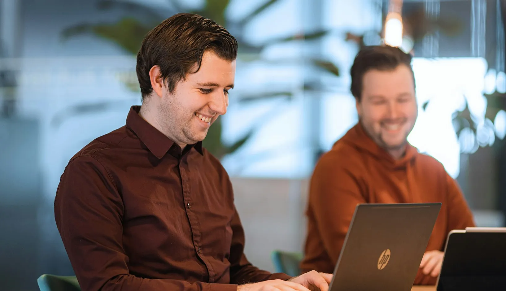 Twee collega's werken lachend op hun laptops