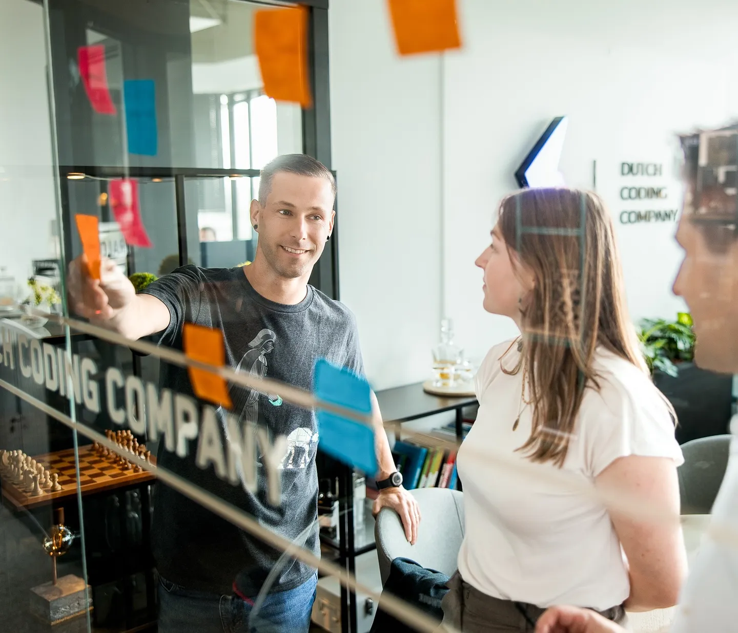 Three colleagues putting sticky notes on a glass wall at Dutch Coding Company